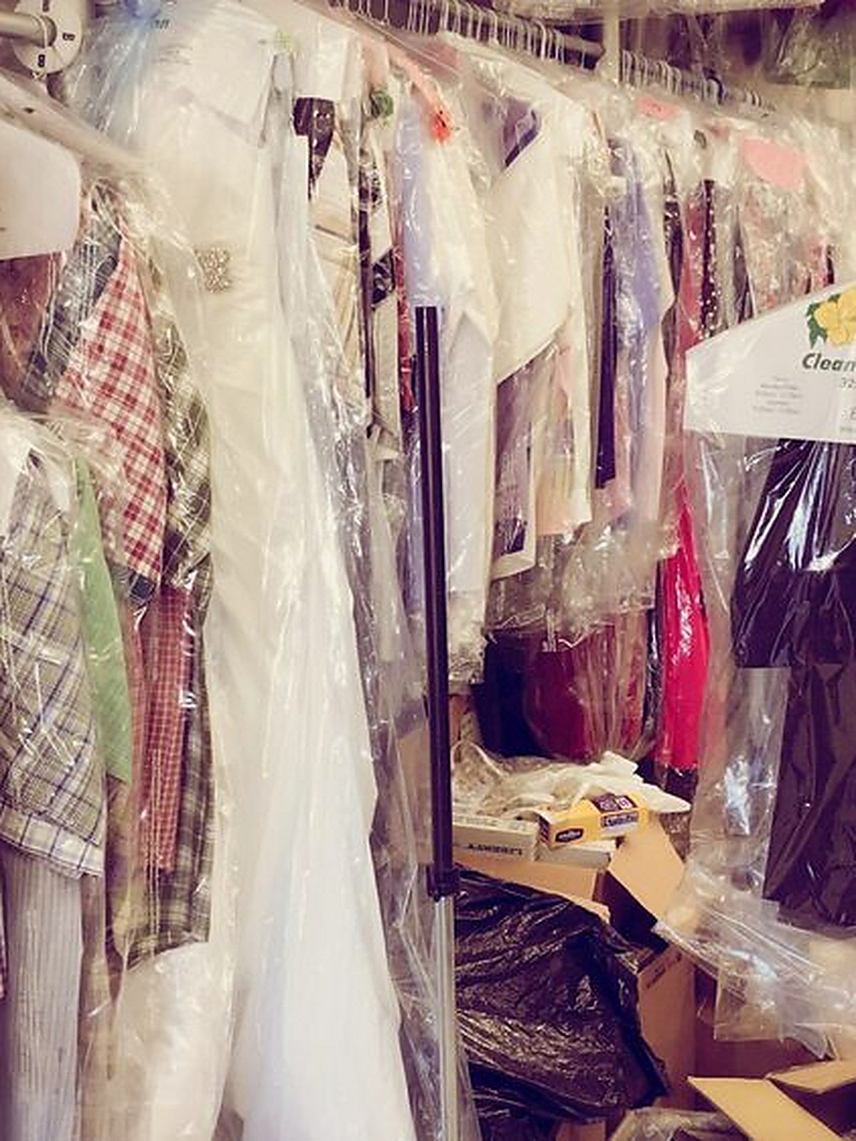 Finished orders on the rack under clear covers, a white bridal gown among them