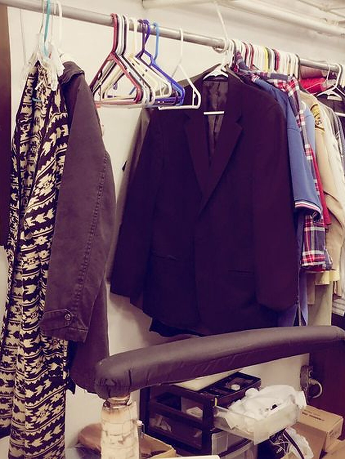 A dark jacket on the rail beside the sleeve board, shirts and a coat waiting behind it